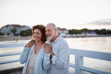 A happy senior couple hugging outdoors on pier by sea, looking at view. - HPIF09281