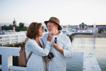 Ein glückliches älteres Paar, das sich im Freien am Pier am Meer umarmt und sich gegenseitig anschaut. - HPIF09286