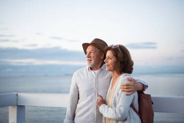 Ein glückliches älteres Paar, das sich im Freien auf einem Pier am Meer umarmt und die Aussicht genießt. - HPIF09294