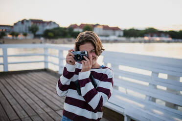 Preteen Mädchen Tourist ein Foto mit Kamera auf Pier am Meer bei Sonnenuntergang, Sommerurlaub Konzept. - HPIF09297