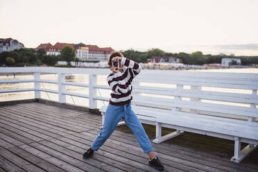 Ein Porträt von preteen Mädchen fotografieren mit Kamera auf Pier am Meer bei Sonnenuntergang, Urlaub Konzept. - HPIF09298