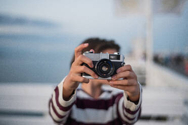 A close up of girl taking photo with camera on pier by sea at sunset, holiday concept. - HPIF09299