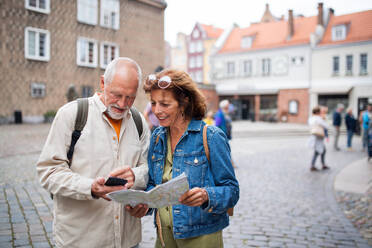 A portrait of happy senior couple tourists using map outdoors in town street - HPIF09319