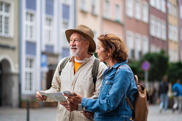 Ein Porträt von glücklichen älteren Paar Touristen mit Karte und Smartphone im Freien in der Stadt Straße - HPIF09321