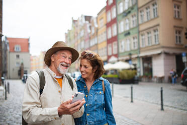 A portrait of happy senior couple tourists using smartphone outdoors in historic town - HPIF09322