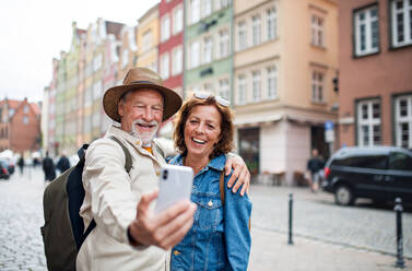 A joyful elderly couple captures a moment with a selfie in a charming historical town during their travels - HPIF09323