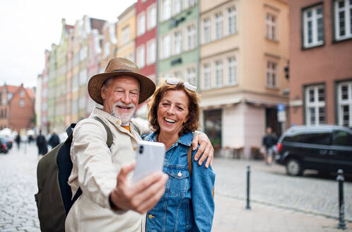 Ein fröhliches älteres Paar hält einen Moment mit einem Selfie in einer charmanten historischen Stadt während ihrer Reise fest - HPIF09323