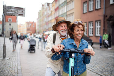 A portrait of happy senior couple tourists riding scooter together outdoors in town - HPIF09325