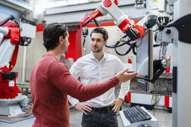 Engineer explaining robotic arm to colleague at industry - DIGF19773