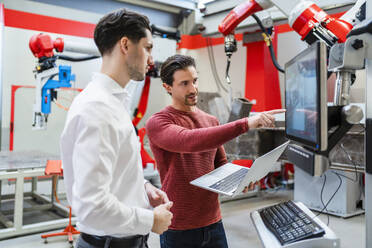 Engineer holding laptop explaining colleague at robot factory - DIGF19782