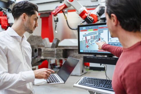 Ingenieur erklärt einem Kollegen in der Roboterfabrik den Laptop - DIGF19786