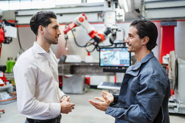 Smiling engineer talking to technician at robot factory - DIGF19788