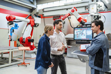 Colleagues discussing together standing at robot factory - DIGF19790