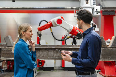 Mature engineer looking at technician holding tablet PC in robot factory - DIGF19809