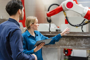 Engineer gesturing and explaining colleague in robot factory - DIGF19813