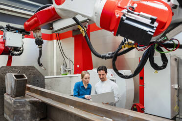 Colleague working over laptop with engineer in robot factory - DIGF19826