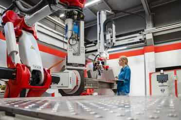 Engineer with laptop looking at robots in factory - DIGF19834