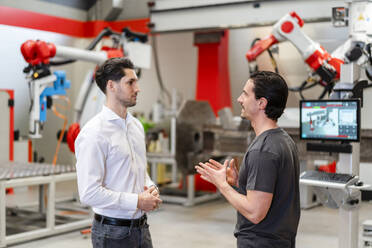 Engineer discussing with colleague standing in robot factory - DIGF19856