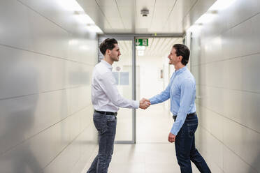 Businessmen doing handshake standing in corridor at factory - DIGF19874