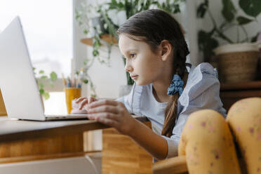 Mädchen mit Laptop am Tisch sitzend im Haus - SSYF00108