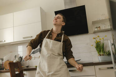 Glücklicher Mann mit Schürze tanzt in der Küche zu Hause - VIVF00426