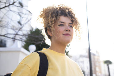 Nachdenkliche junge Frau mit lockigem Haar an einem sonnigen Tag - AMWF01197