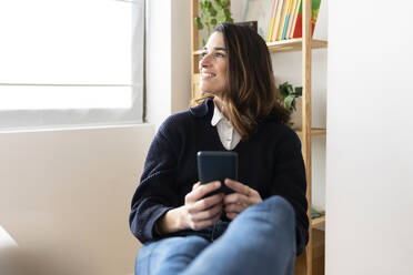Lächelnde Geschäftsfrau sitzt mit Smartphone im Büro - XLGF03269