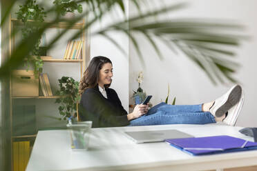 Happy businesswoman using mobile phone at desk - XLGF03270