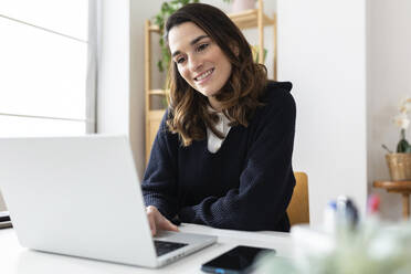 Happy businesswoman using laptop at desk - XLGF03276