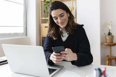 Smiling businesswoman using mobile phone at desk - XLGF03278