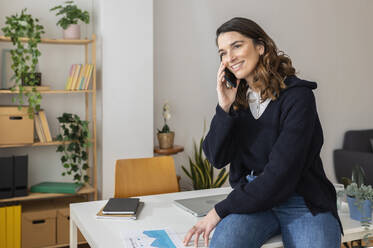 Smiling businesswoman talking on smart phone and sitting at desk - XLGF03288