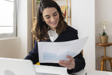 Smiling businesswoman examining graph at desk - XLGF03290