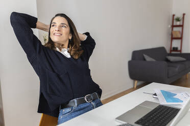 Happy businesswoman with hands behind head sitting at desk - XLGF03293