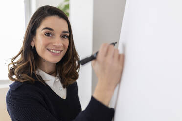 Glückliche Geschäftsfrau mit Filzstift, die auf einem Flipchart schreibt - XLGF03296