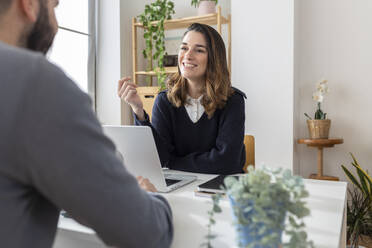 Happy businesswoman having discussion with colleague at desk - XLGF03303