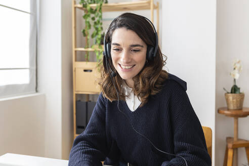 Happy businesswoman wearing headset sitting at desk - XLGF03307