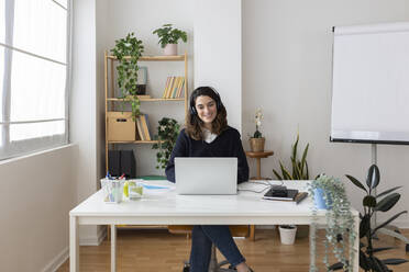 Smiling businesswoman wearing headset using laptop in office - XLGF03308