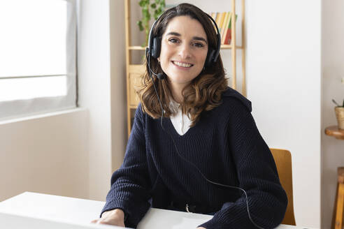 Happy businesswoman wearing headset at desk - XLGF03310