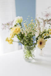Gelbe und weiße Blumen in Glasvase auf Tisch - ONAF00422