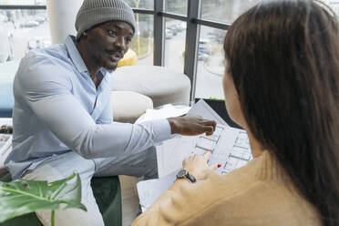 Young architect discussing with colleague over documents at office - OSF01418