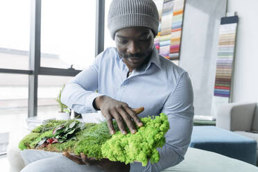 Young interior designer touching sample of green wall at office - OSF01425