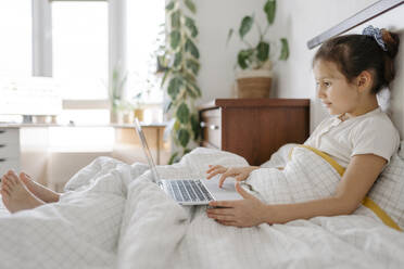 Nettes Mädchen mit Laptop auf dem Bett im Schlafzimmer - SSYF00114