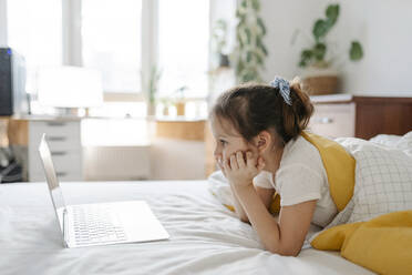 Mädchen beobachtet Laptop auf dem Bett liegend im Schlafzimmer zu Hause - SSYF00116