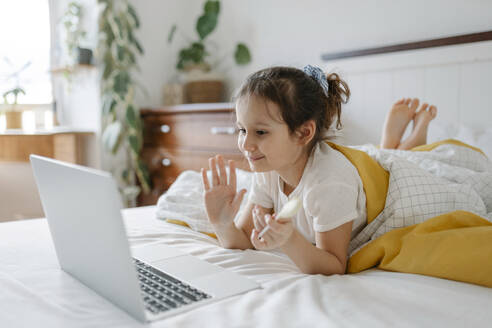 Lächelndes Mädchen winkt bei einem Videoanruf über einen Laptop zu Hause - SSYF00117