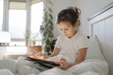 Girl using tablet PC sitting in bedroom - SSYF00118