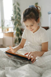 Smiling girl using tablet computer in bedroom at home - SSYF00119