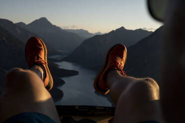 Sportschuhe eines Mannes, der bei Sonnenuntergang auf einem Berg sitzt - MALF00432