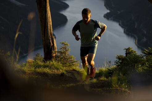 Entschlossener Sportler joggt bei Sonnenuntergang auf einem Berg - MALF00435