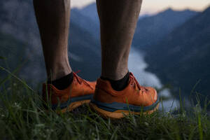 Man wearing sports shoes standing on grass looking at mountains - MALF00441