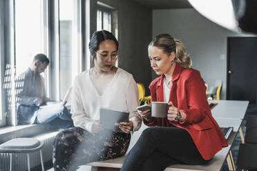 Geschäftsfrauen, die drahtlose Technologien am Schreibtisch im Büro nutzen - UUF28376